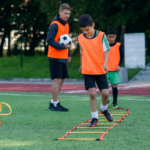 two-school-boys-are-running-ladder-drills-turf-football-summer-camp-intense-soccer-training-with-coach (1)
