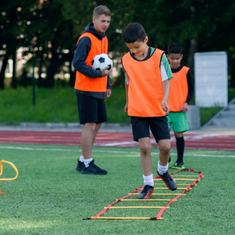 two-school-boys-are-running-ladder-drills-turf-football-summer-camp-intense-soccer-training-with-coach (1)
